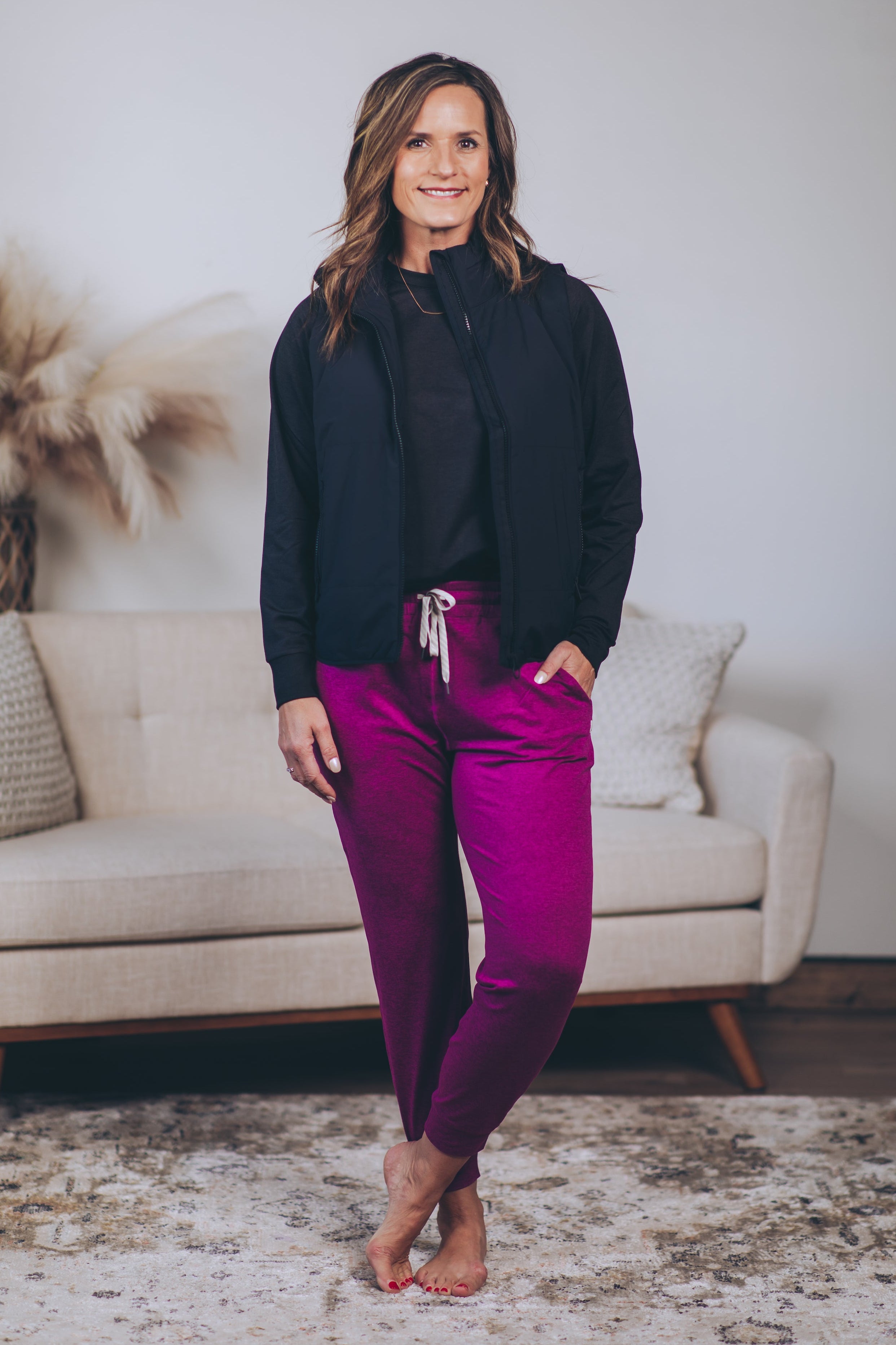 Woman in a living room wearing a black jacket and bright magenta pants.