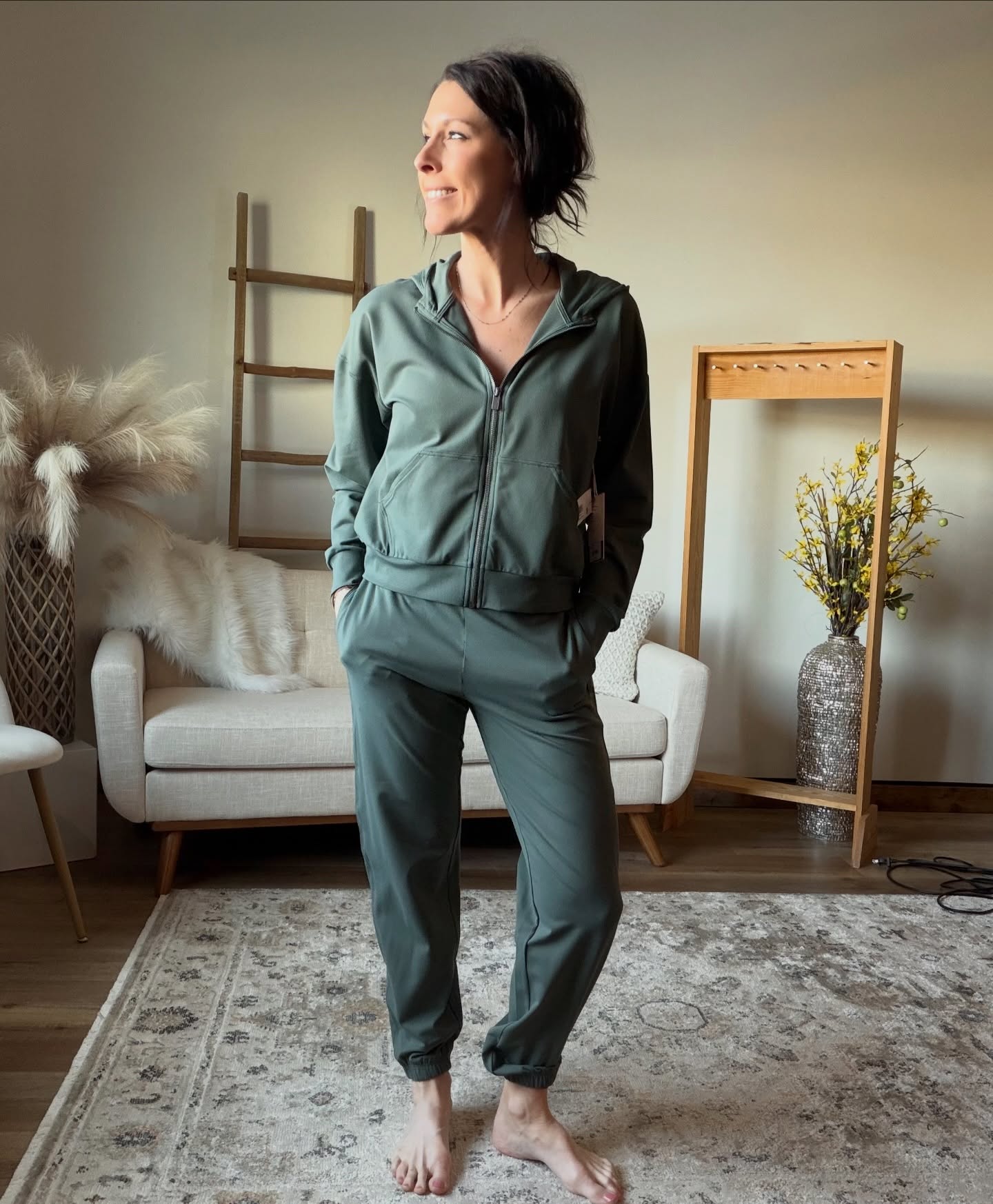 Woman in a green tracksuit standing in a living room with a white sofa and decorative items.